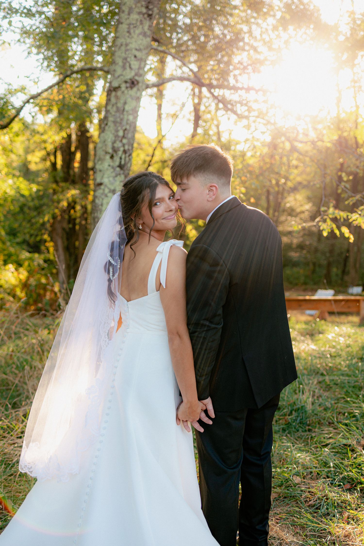 Bride and groom sharing tender kiss in golden sunset forest light.