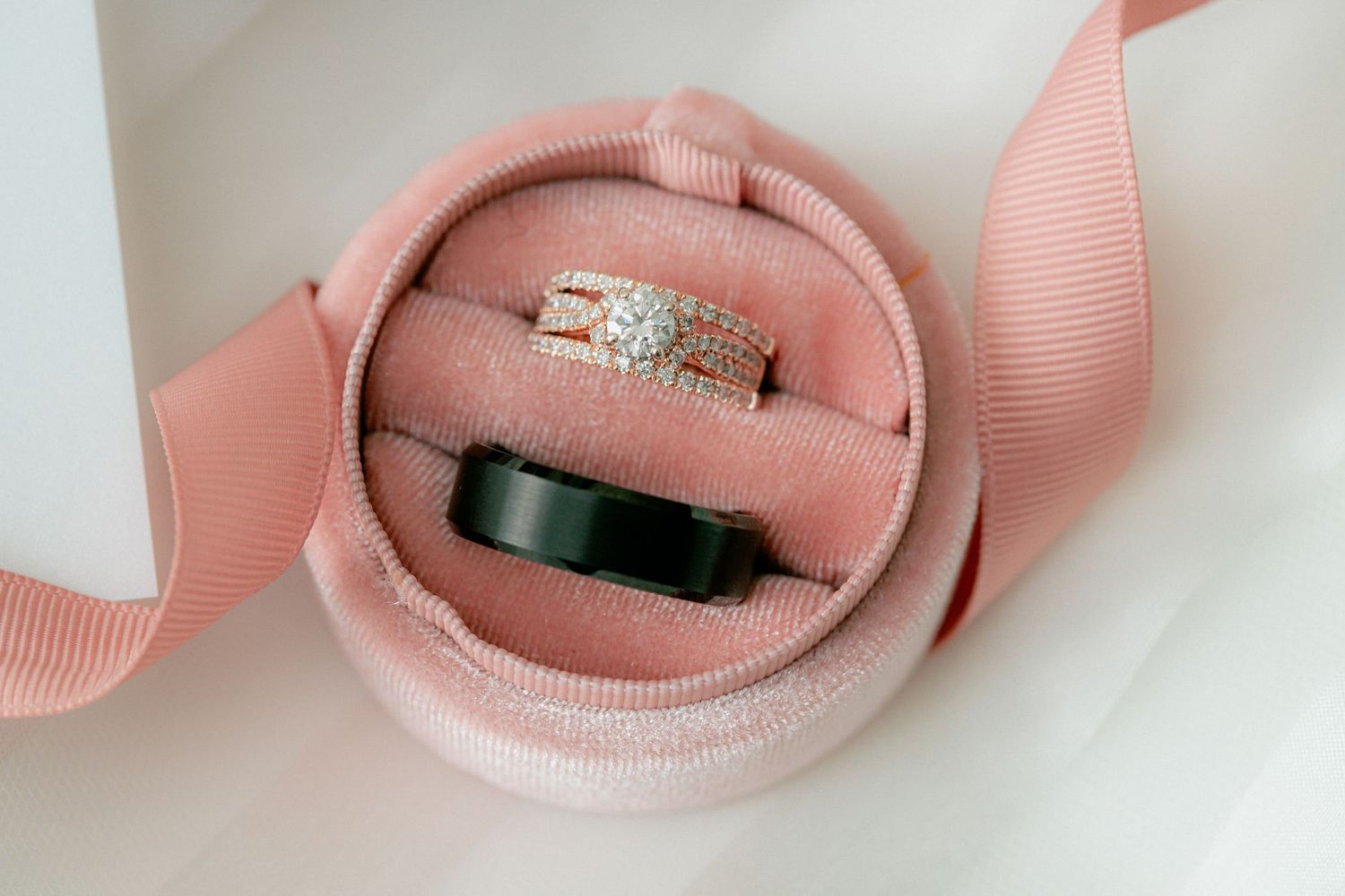Wedding rings displayed in a pink velvet ring box with a gold diamond band and black groom ring.