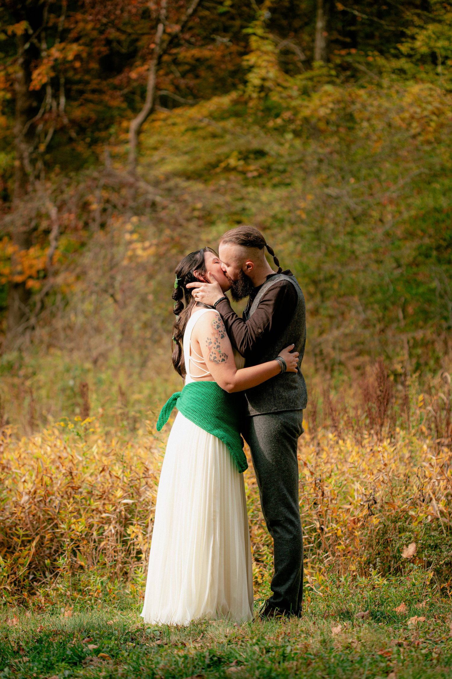 Bride and groom share a first kiss surrounded by vibrant autumn foliage during outdoor fall wedding.