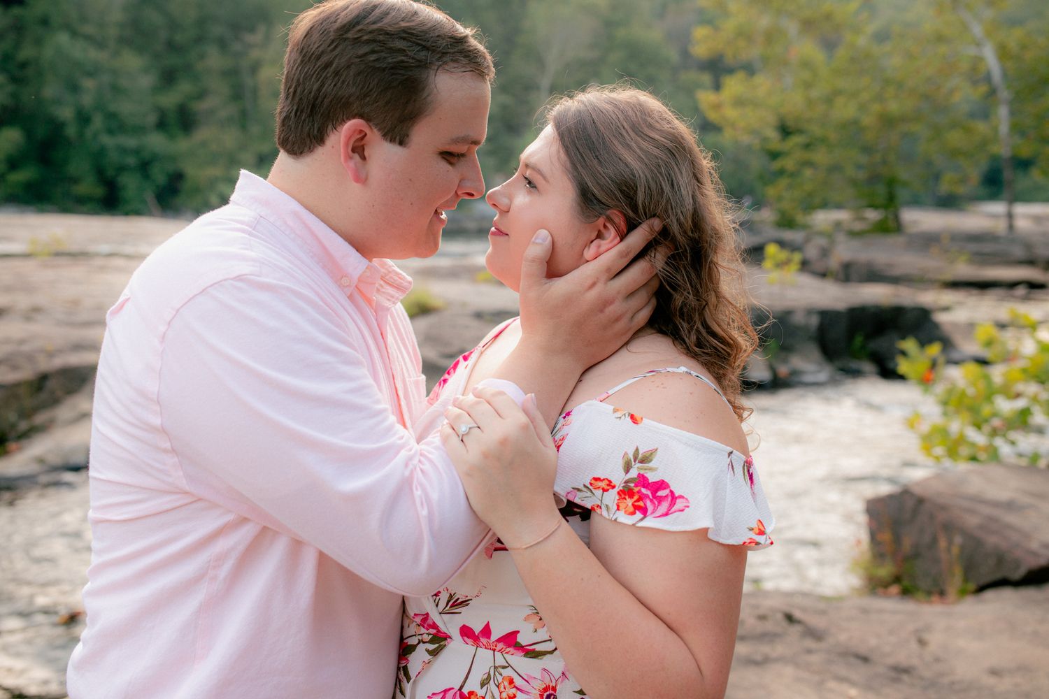 Couple sharing a romantic moment near rocky waterfall, groom tenderly cupping bride's face.