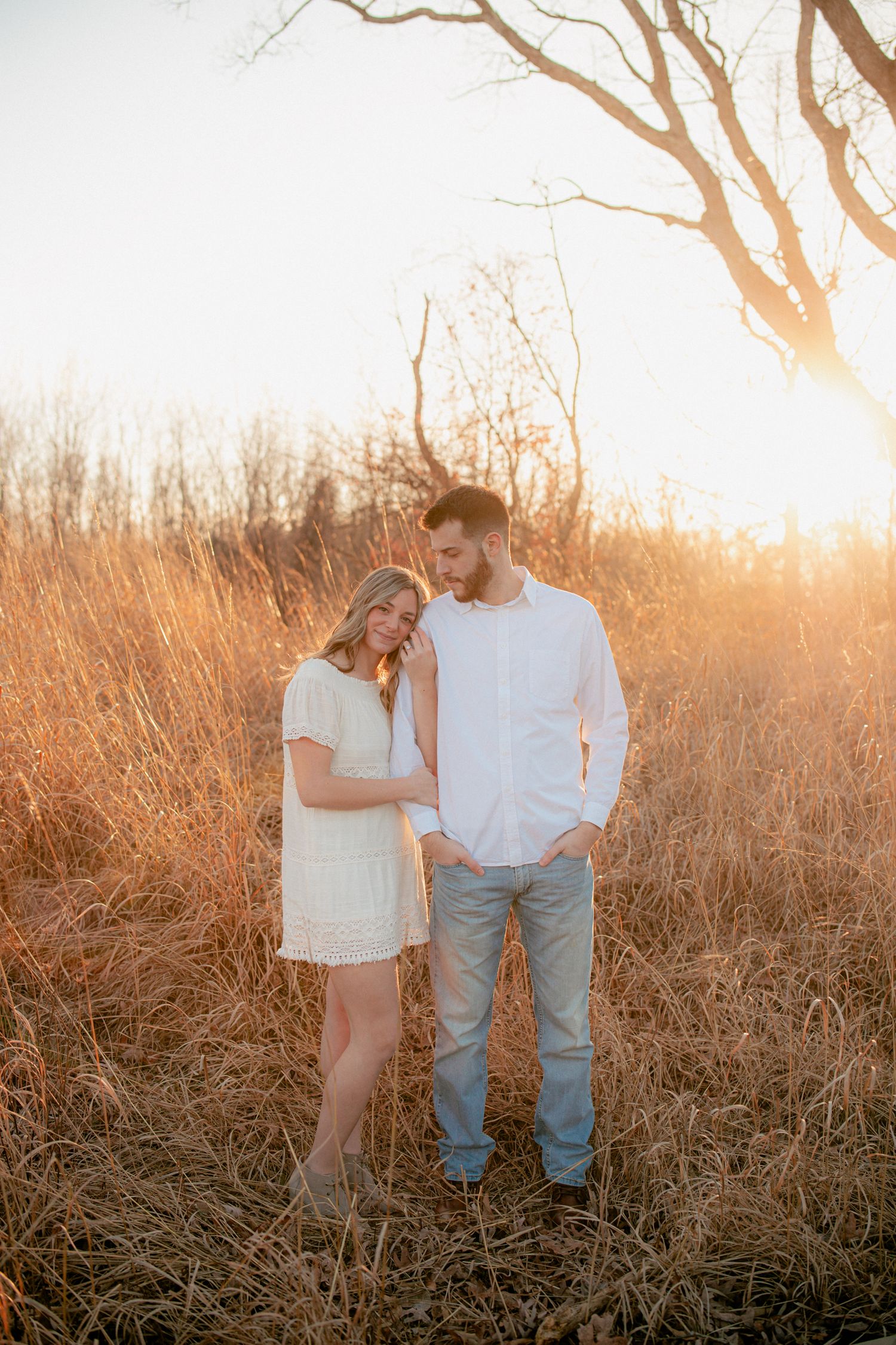Couple embracing in golden tall grass field during romantic sunset engagement photo session.