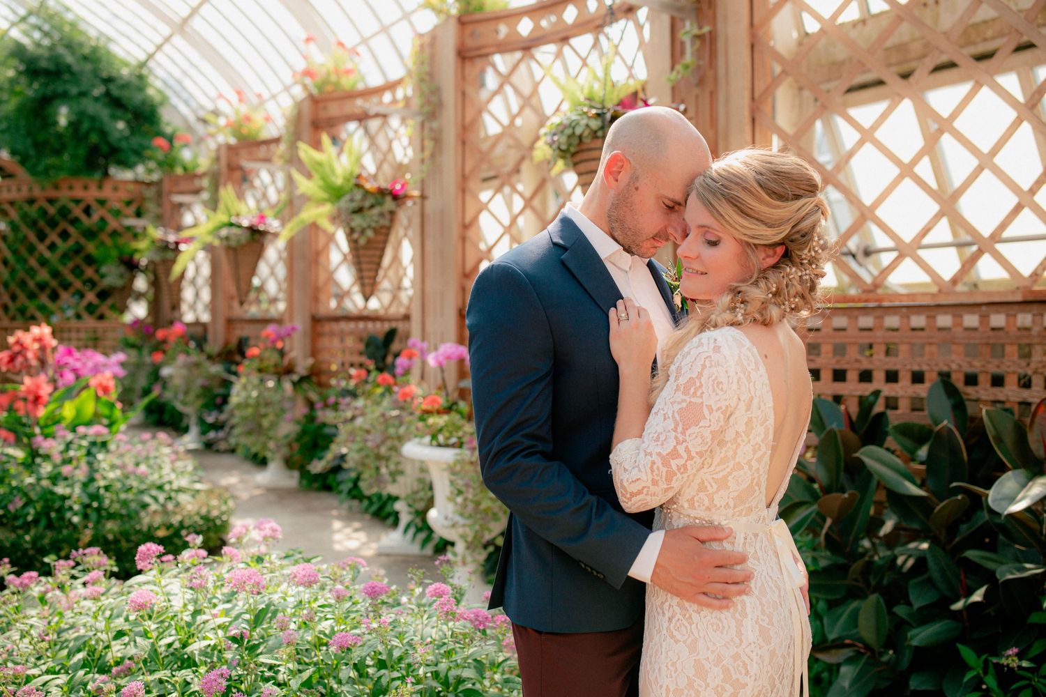 Bride and groom share an intimate embrace inside a sunlit botanical greenhouse.
