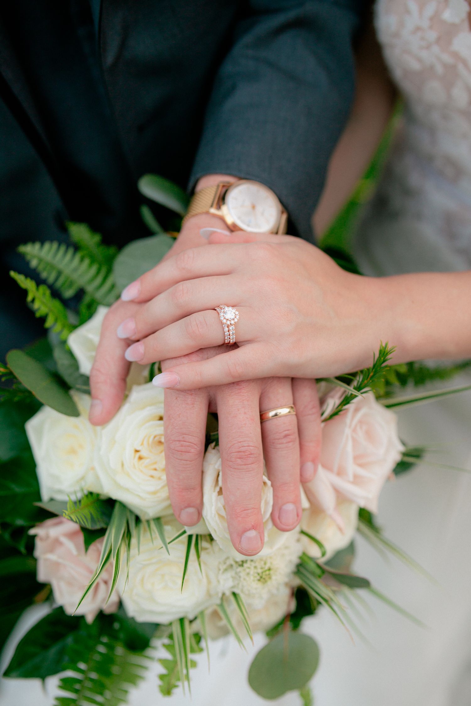 Newlyweds show off wedding bands resting hands on white rose bridal bouquet.