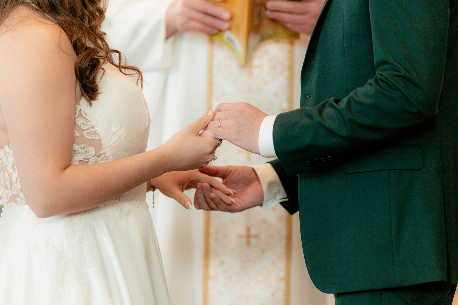Bride placing wedding ring on groom's finger during ceremony, groom wearing emerald green suit.