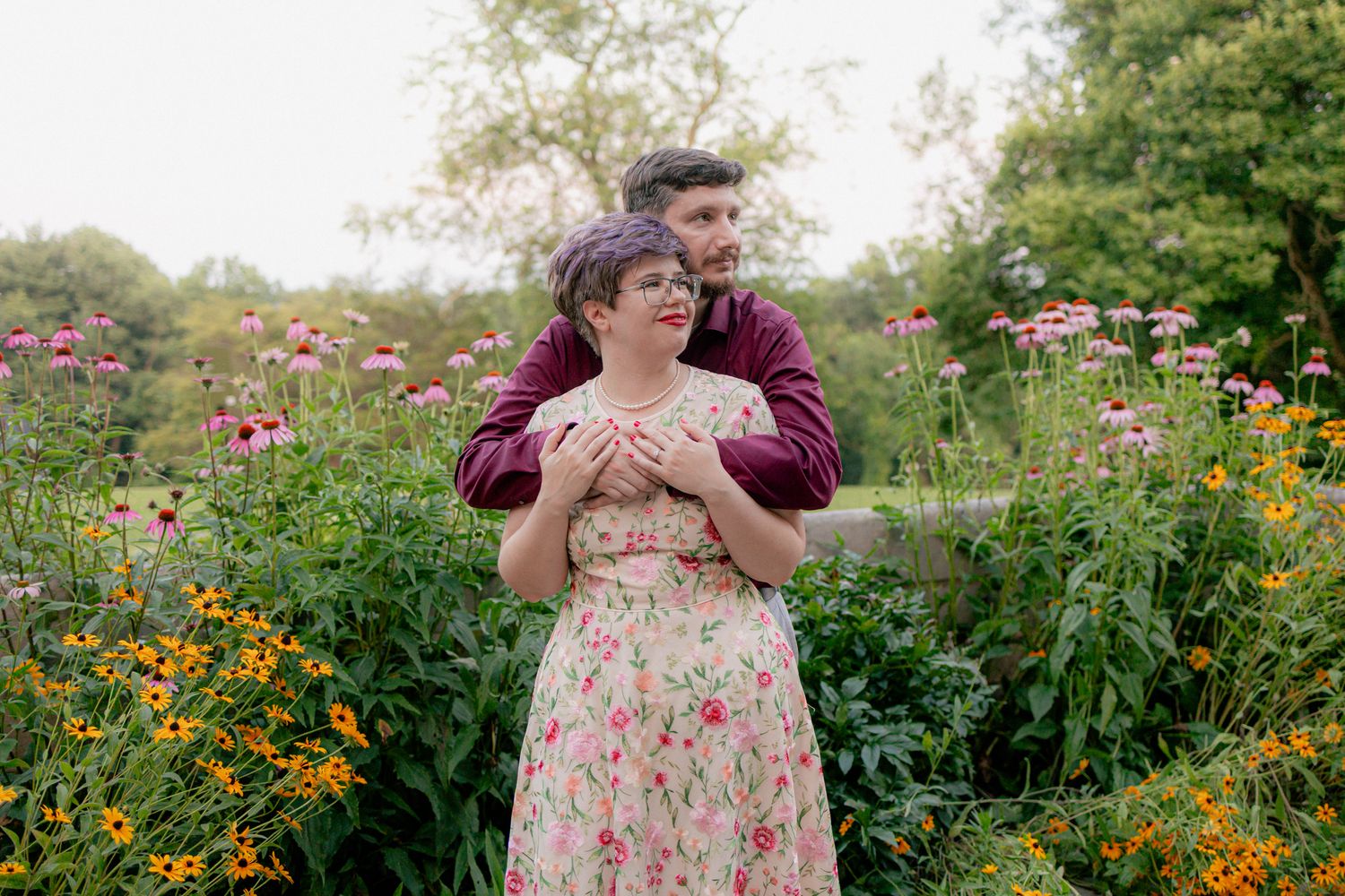 Couple embracing in a vibrant garden filled with colorful wildflowers in soft summer light.