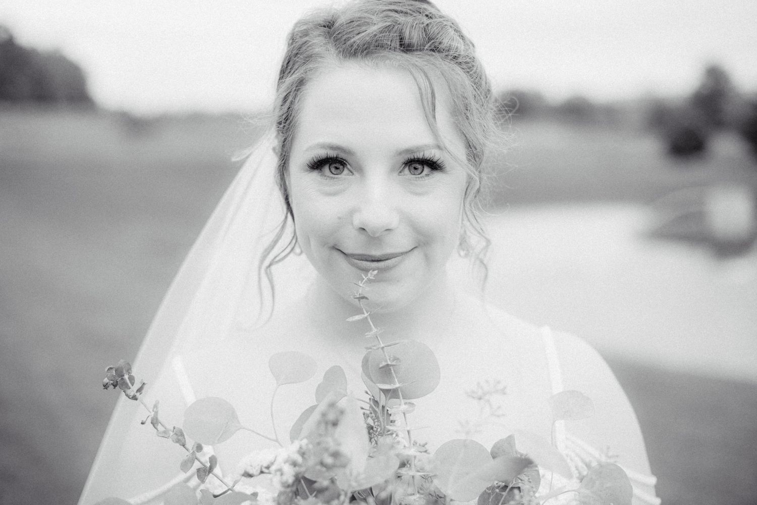 Elegant black and white bridal portrait of smiling bride in veil holding floral bouquet.