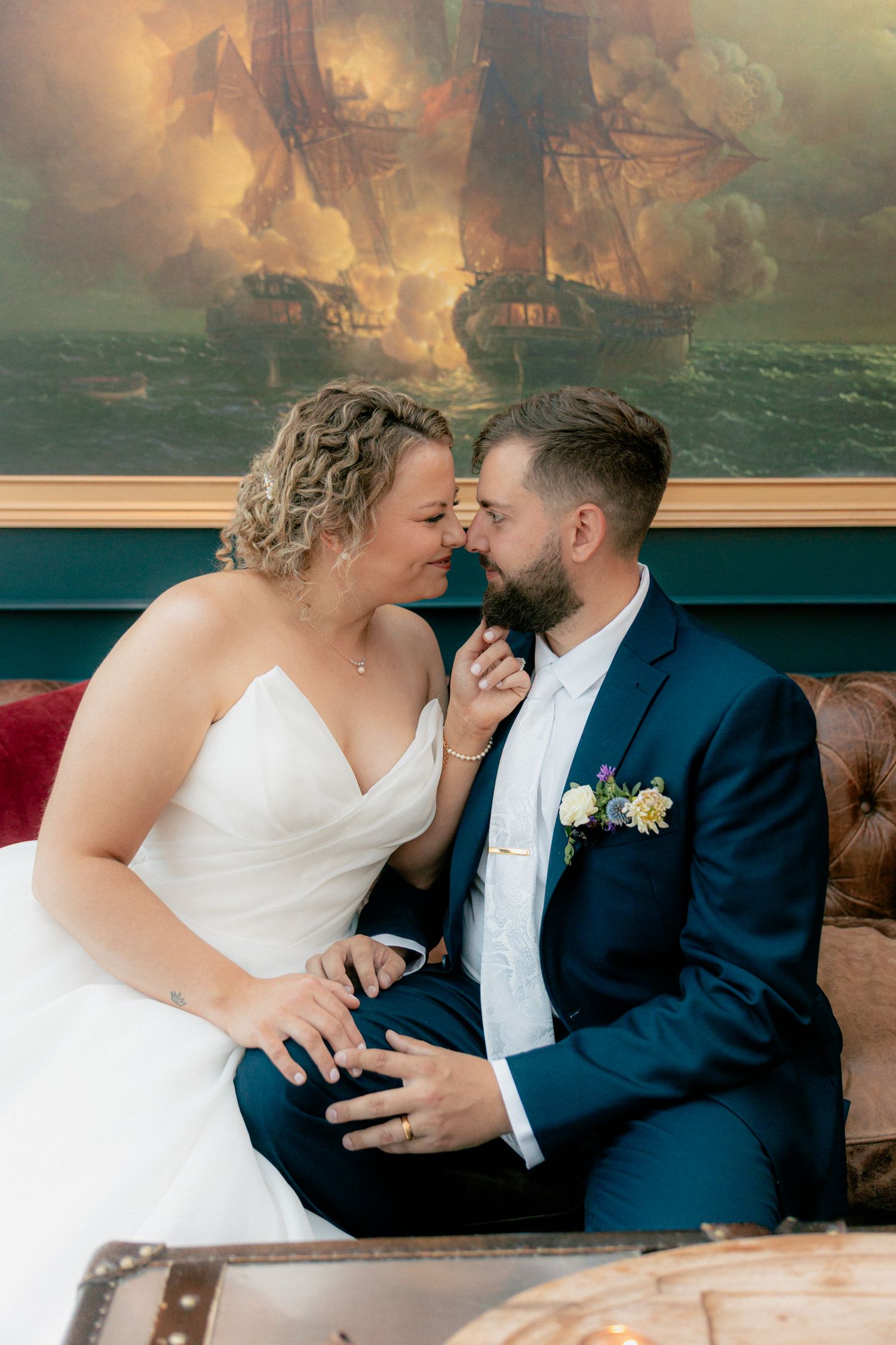 Bride and groom sharing intimate moment on sofa before nautical painting.