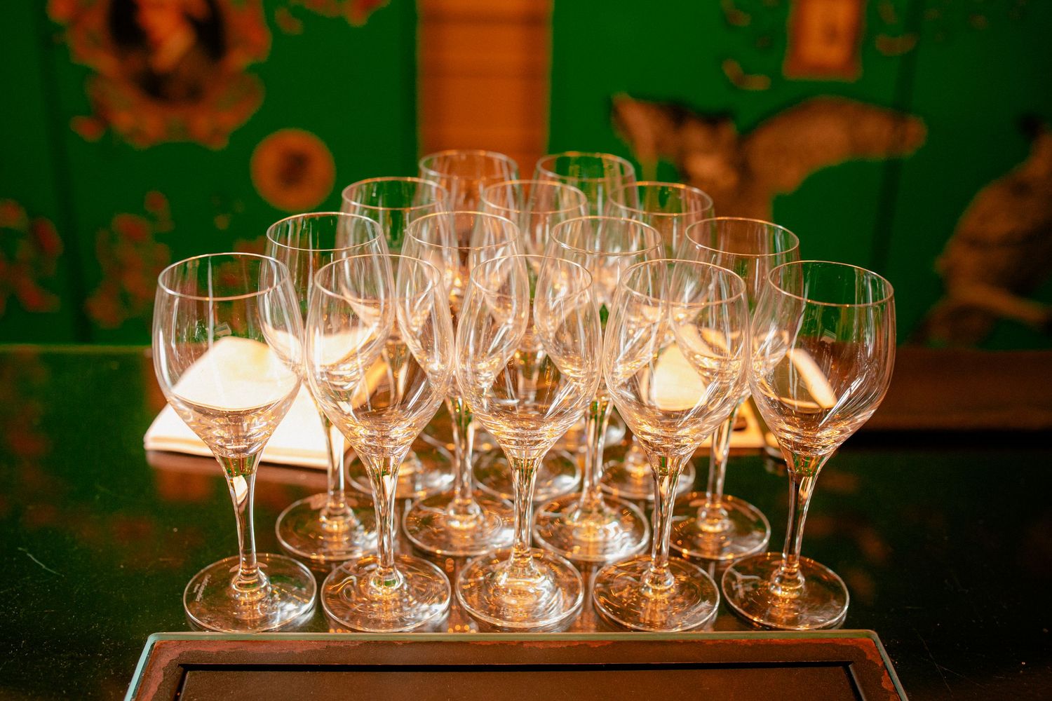 Elegant crystal wine glasses arranged in rows on a tray against a vibrant green decorative background.