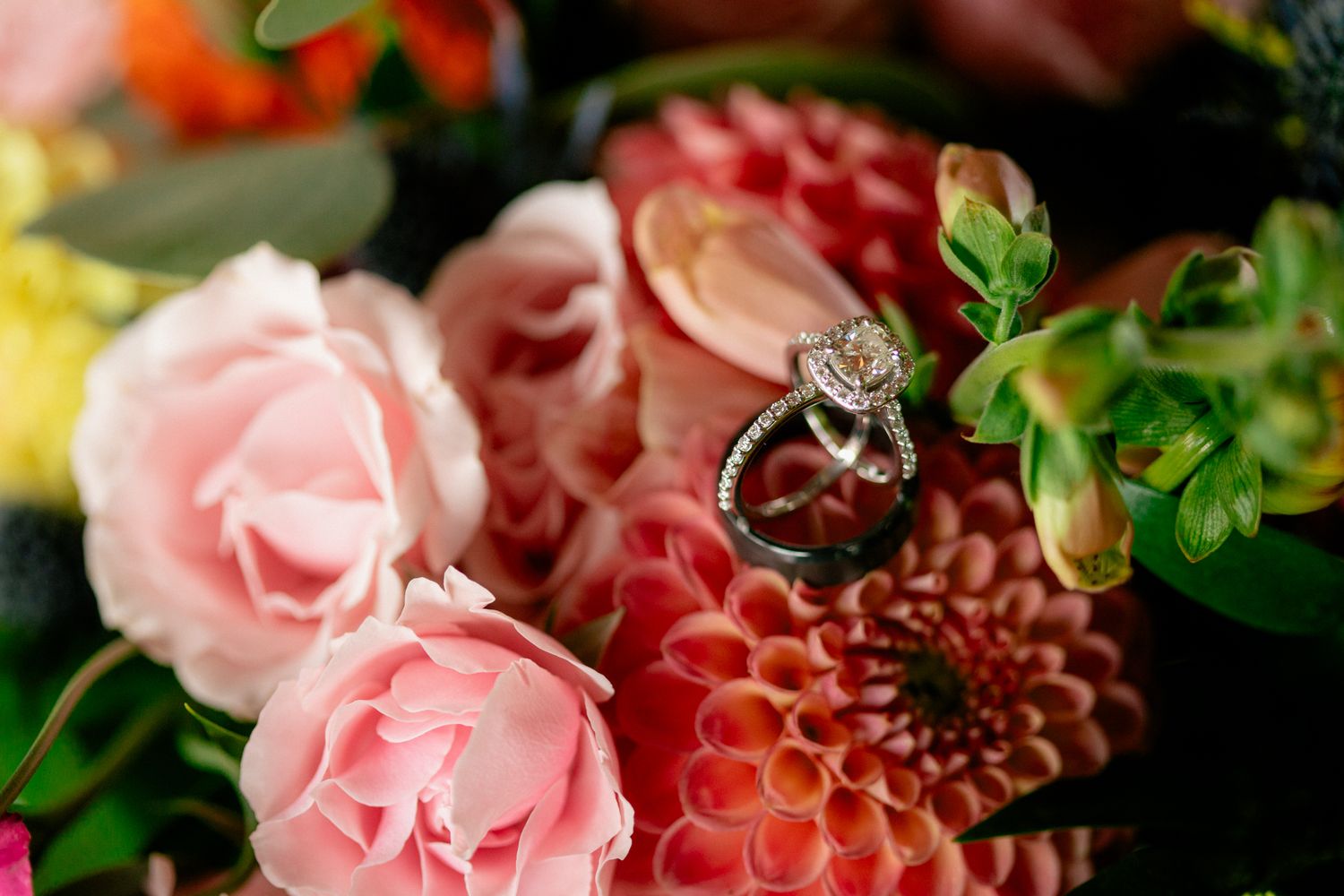 Diamond engagement ring displayed on vibrant pink dahlias and roses in a colorful bouquet.