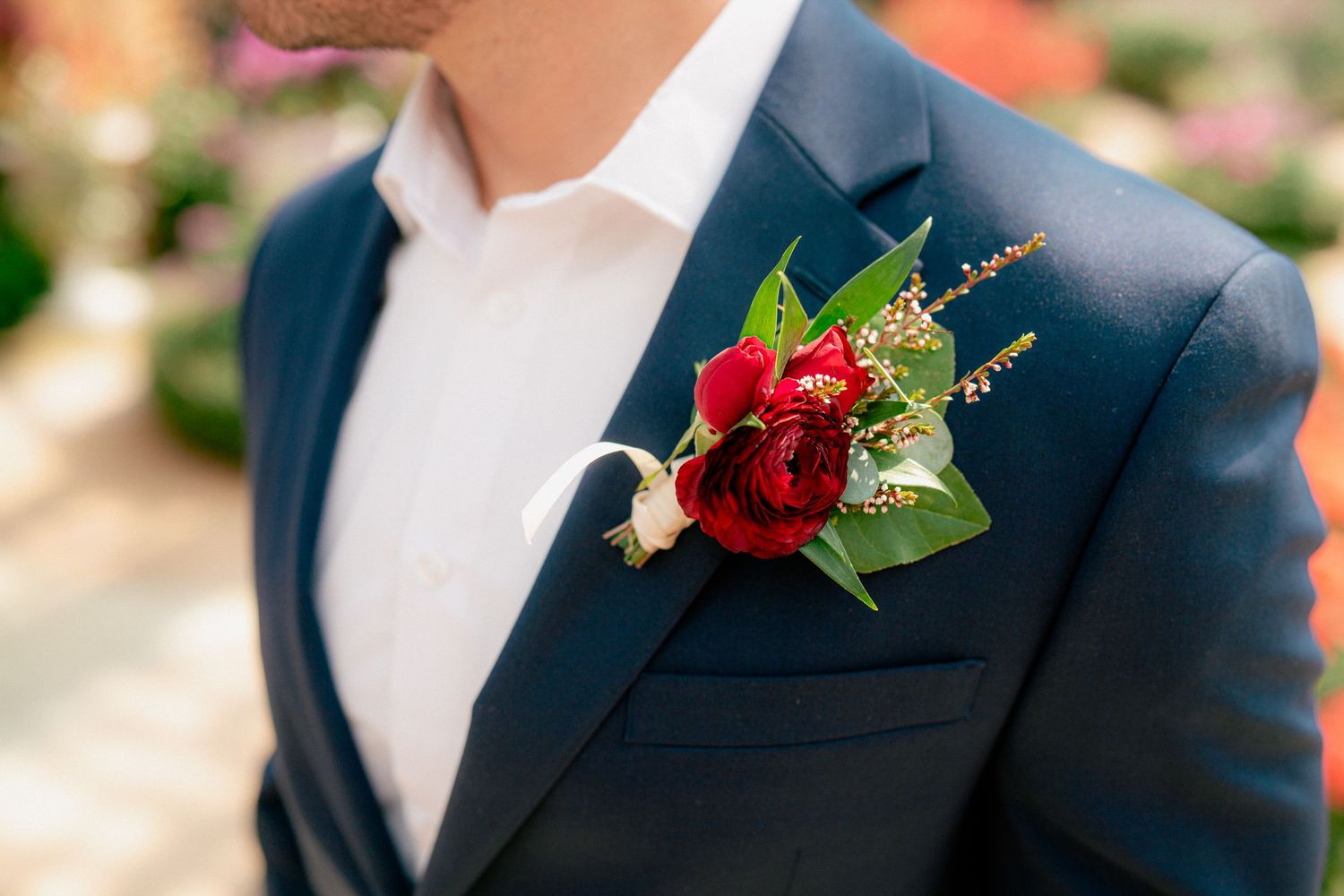 Close-up of groom's elegant navy suit with deep red rose and greenery boutonniere.