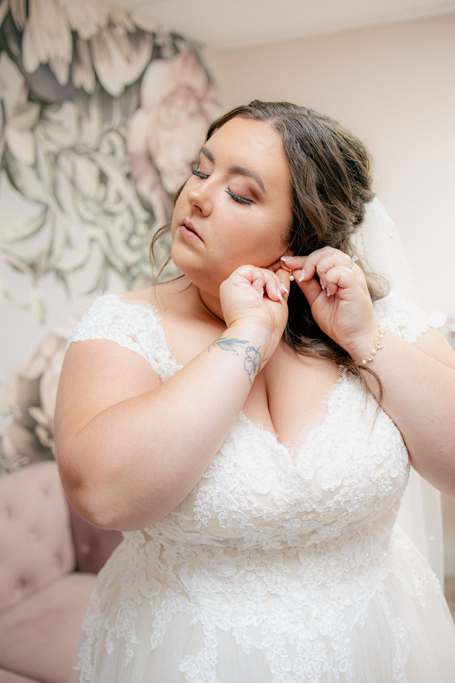 Bride in a lace wedding gown puts on earrings while getting ready before her wedding ceremony.