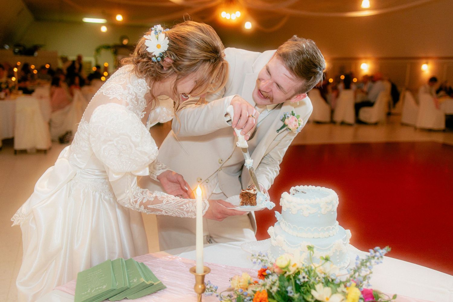 Bride and groom laugh together while cutting their white wedding cake at the reception.
