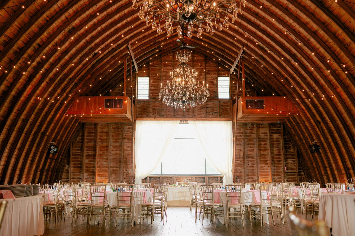 Rustic barn wedding venue with chandelier, string lights, and elegant table settings for a reception.
