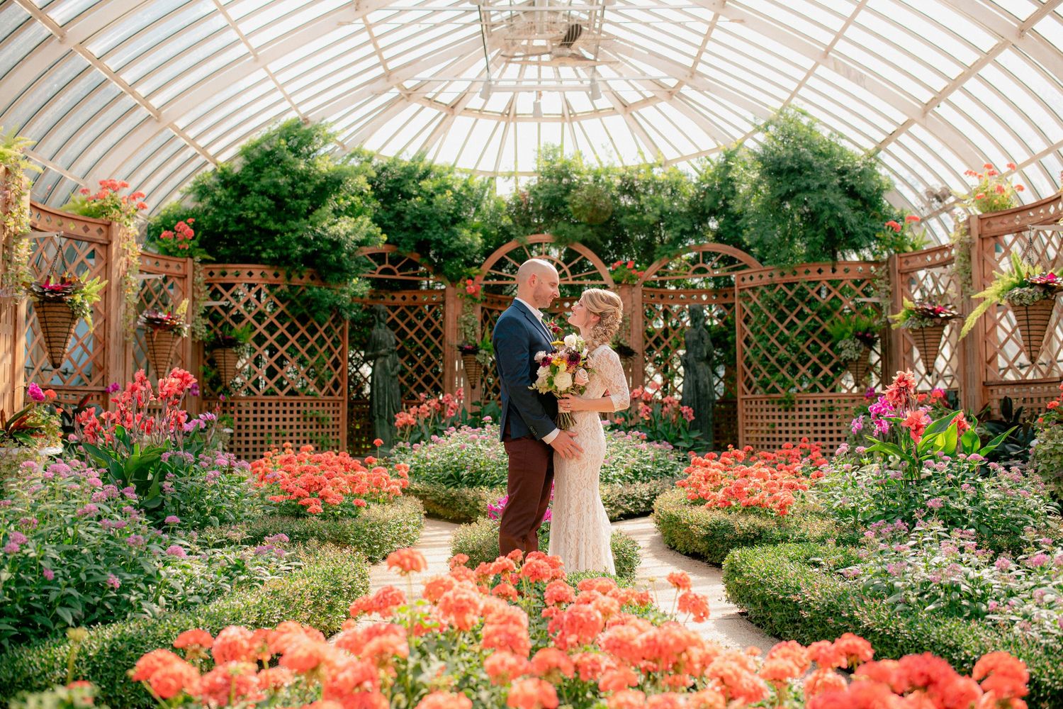 Bride and groom share a romantic moment surrounded by vibrant flowers in a greenhouse.