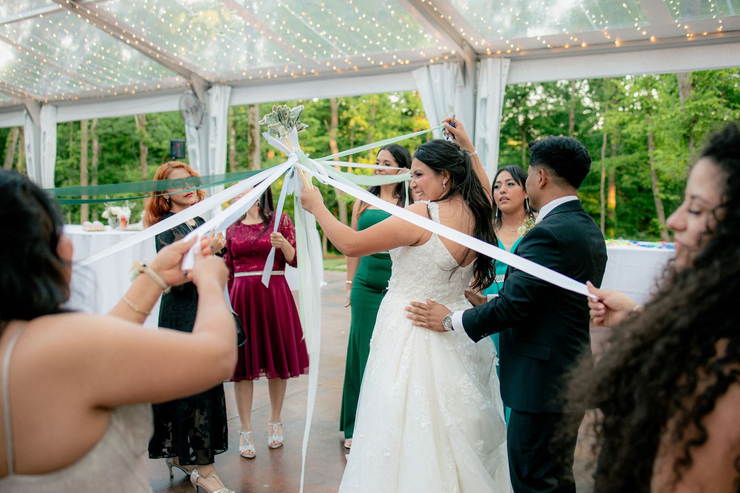 Bride and groom walk through ribbon tunnel created by wedding guests during outdoor reception.