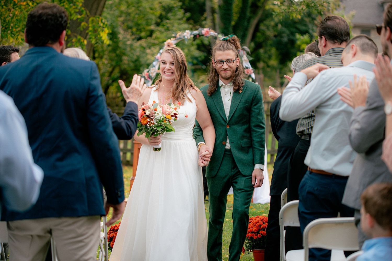 Bride and groom walk down the aisle hand in hand, smiling at guests during outdoor wedding ceremony.