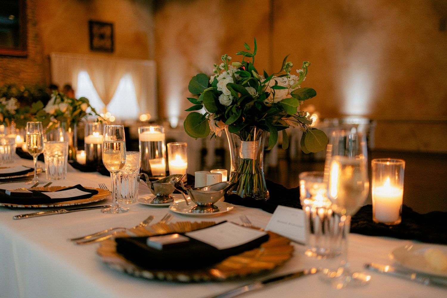 Romantic candlelit wedding reception table with greenery centerpiece, gold chargers, and glowing candles.