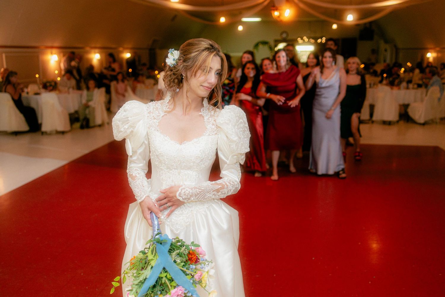 Elegant bride in a long-sleeved gown prepares to toss her colorful bouquet at the wedding reception.