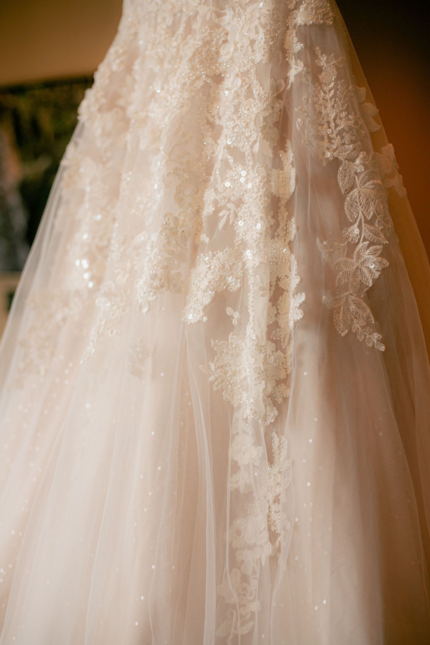 Close-up detail of intricate lace and beaded embroidery on a flowing champagne wedding ball gown.