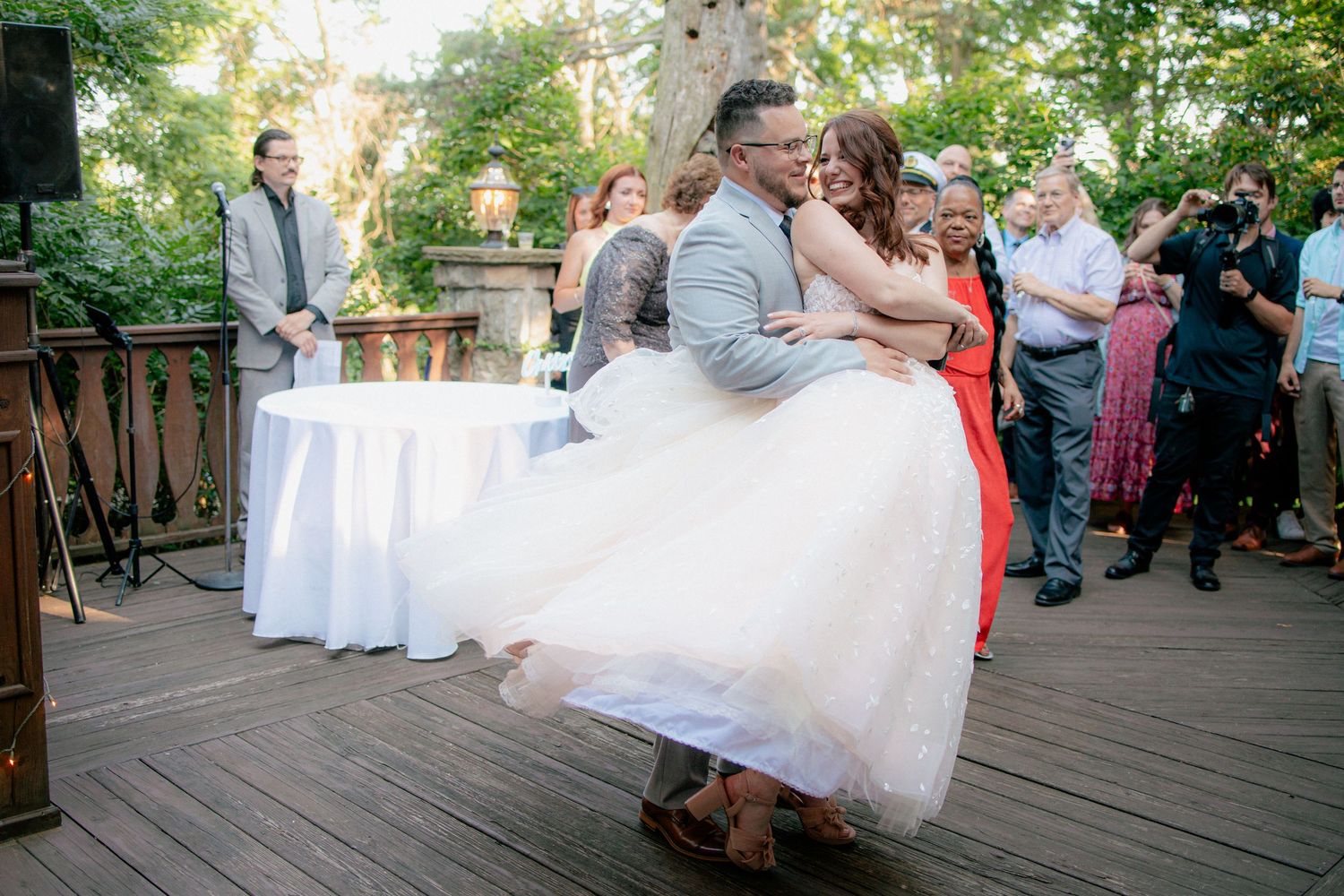 Groom in gray suit lifting and kissing bride in white gown during first dance on outdoor deck.