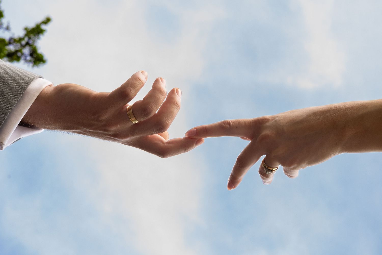 A view looking up towards the sky of two hands reaching towards each other, fingertips touching