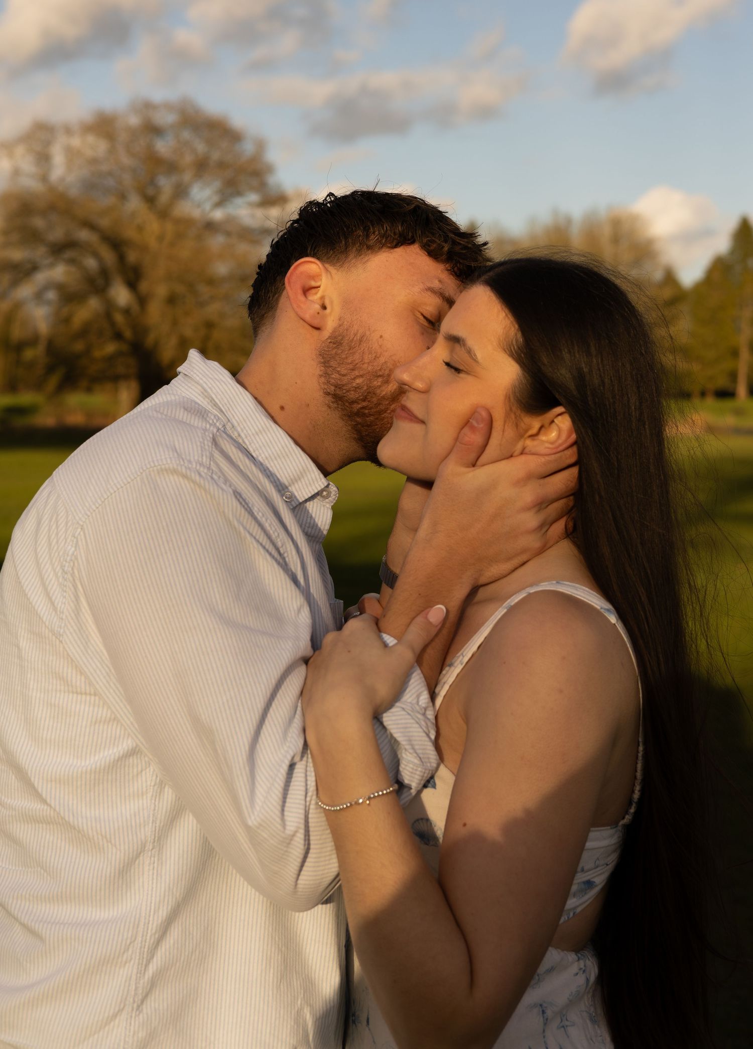 A side profile image of a man holding a woman's face and kissing her on the cheek while she smiles