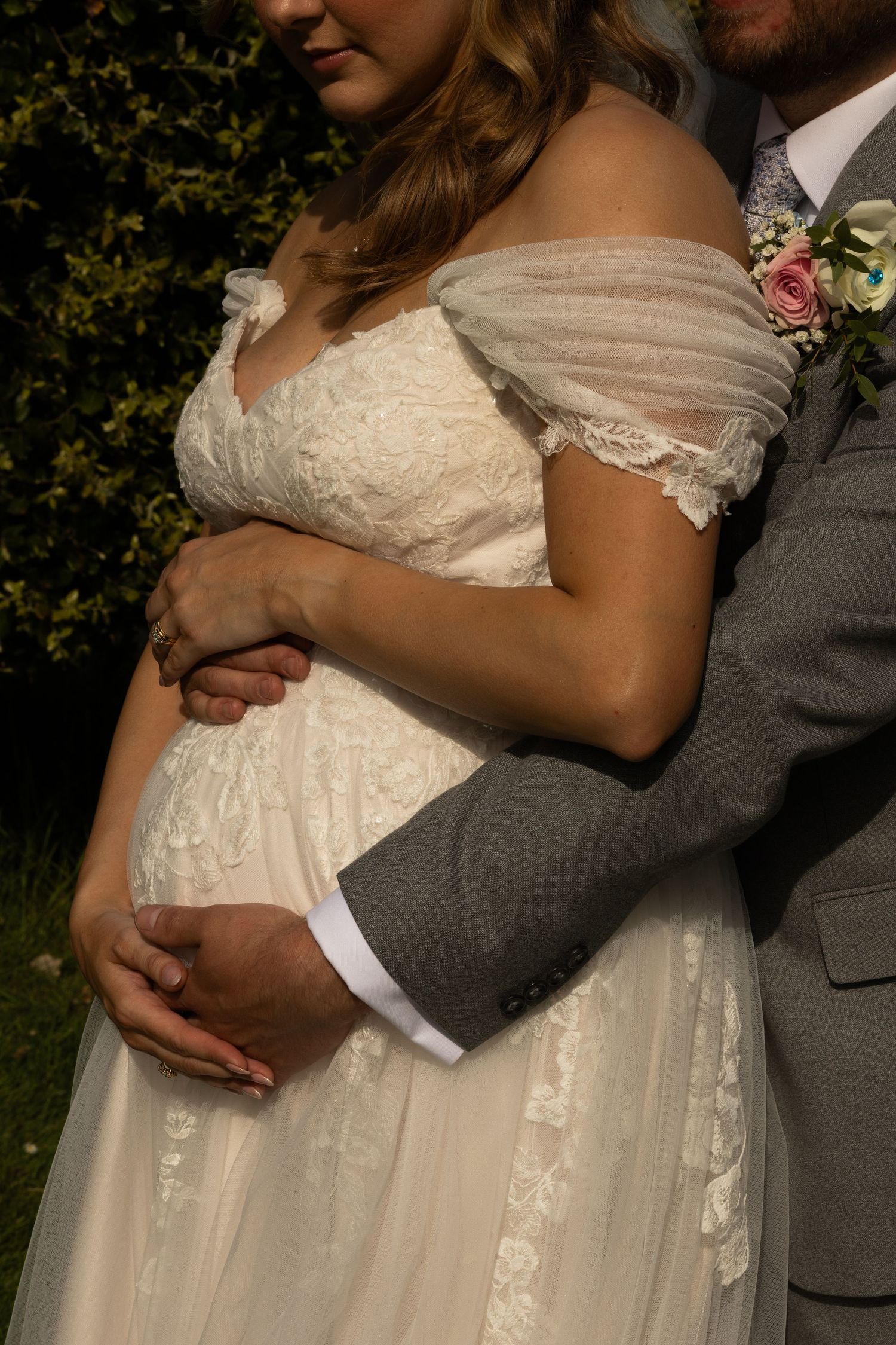 A close up side view of a groom holding the bridge bump from behind