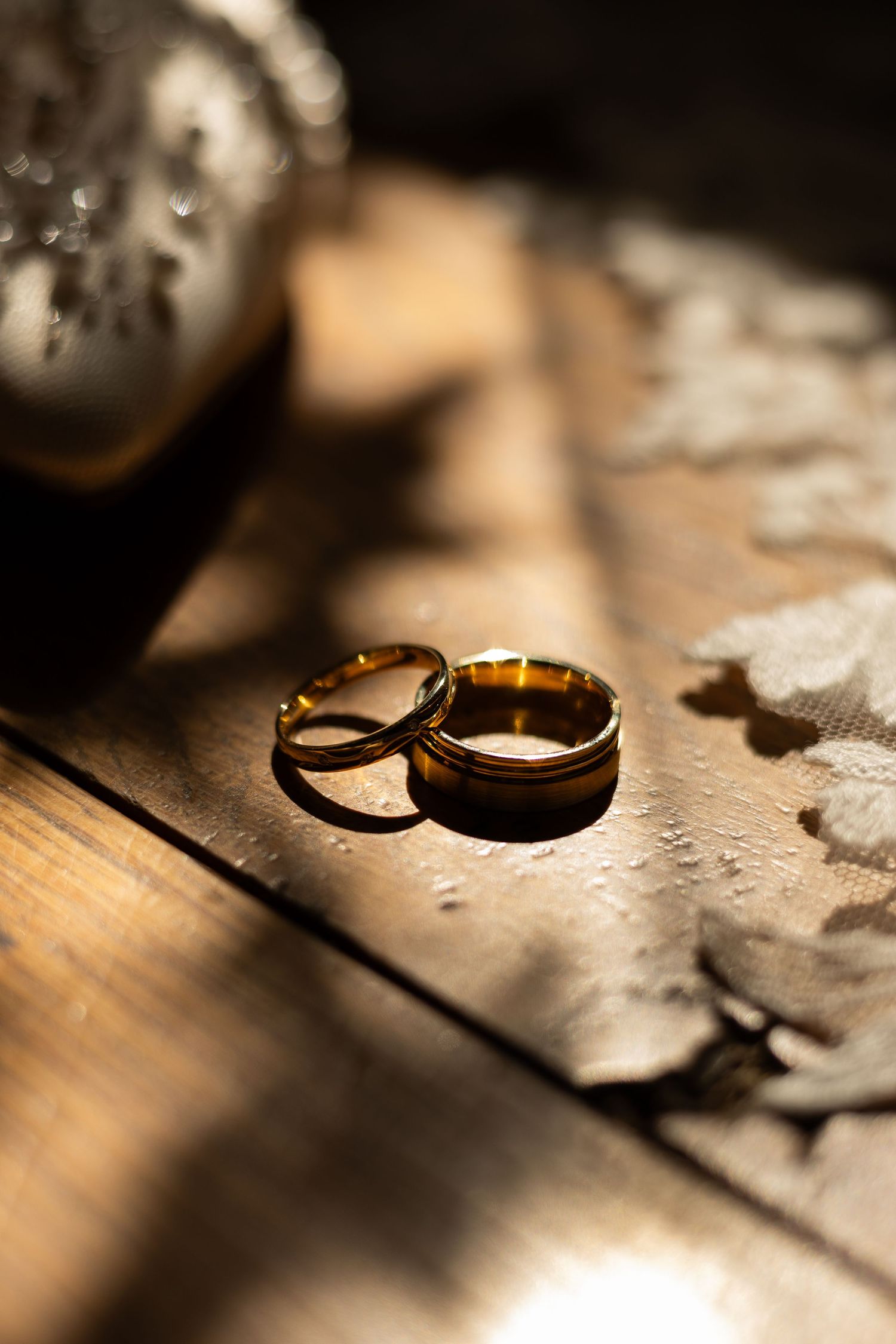 A close up image of the bridge and grooms wedding rings placed together next to a veil and some shoes