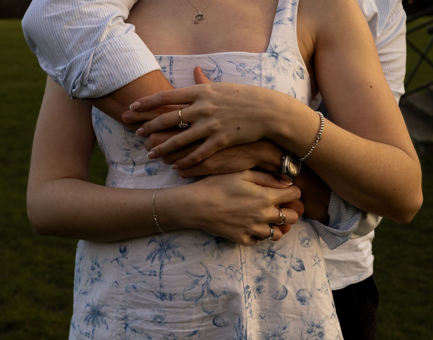 A man stood behind a woman he wraps her arms around her and they hold hands. The photograph just shows their torsos.