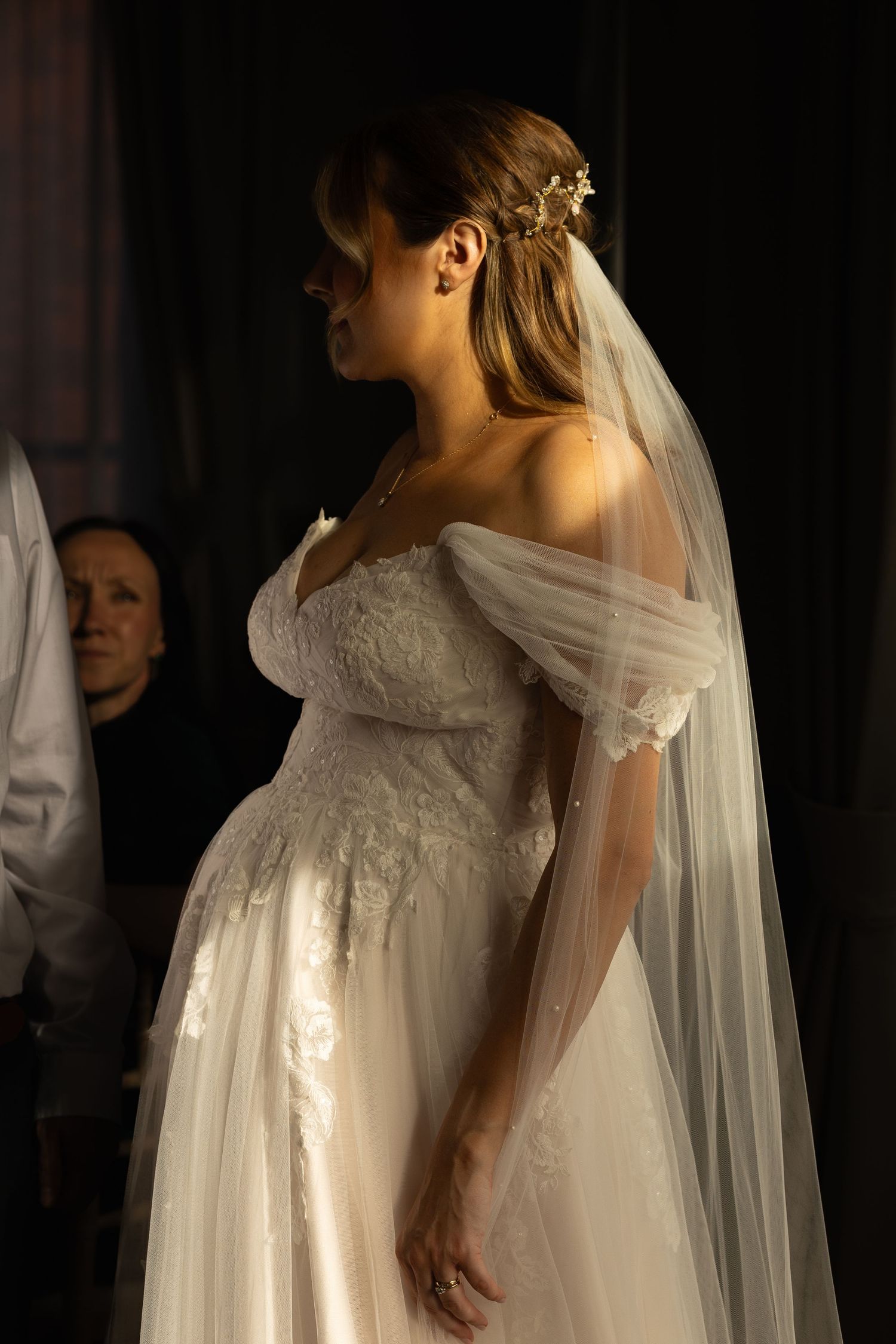 A side view of a bride looking into the distance in front of a window with the sunlight streaming in behind her
