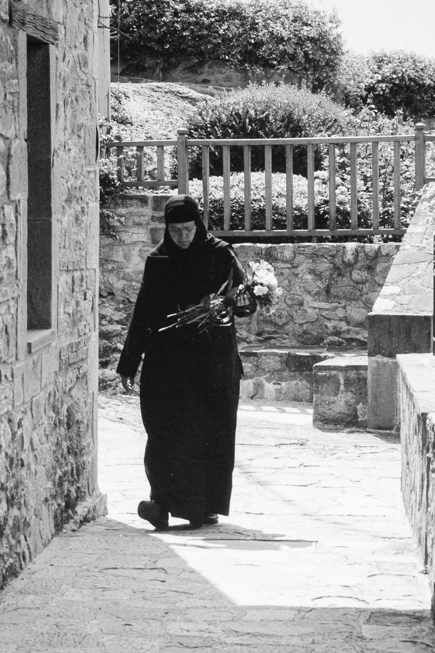 black and white sliver gelatin print of religious order member carrying freshly cut flowers at Meteora monastery, Greece