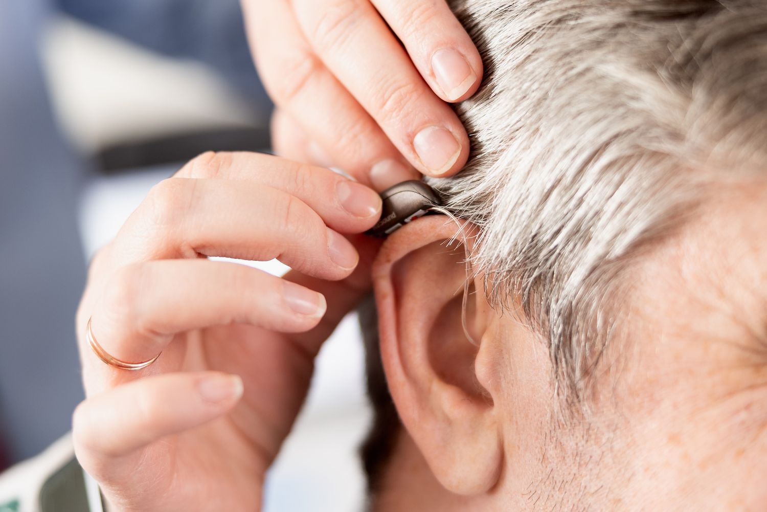 A close up photo of a hearing aid being applied to an elderly patient. Commerical lifestyle photography, elderly, bright, hearing, medical.