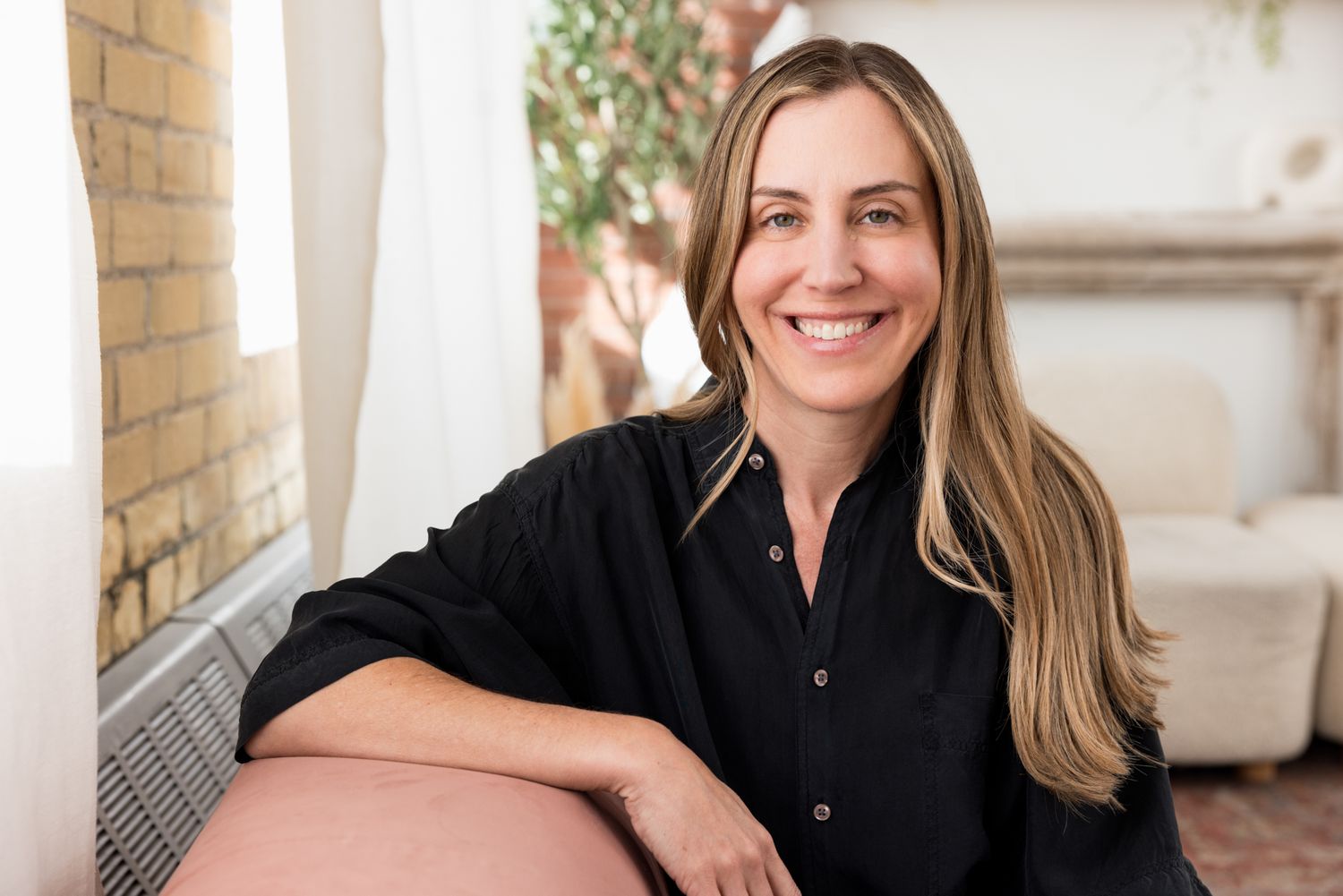 A middle aged white woman with blond hair relaxes on the couch, looking at the camera. Light, Commercial lifestyle photography.