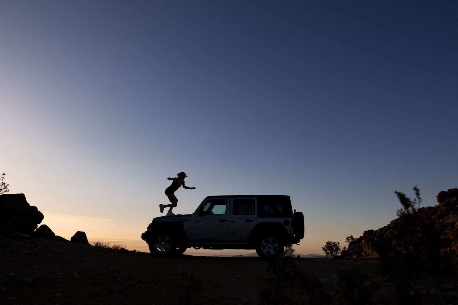A young person climbs atop a jeep at sunset in joshua tree desert, travel adventure documentary fun photography