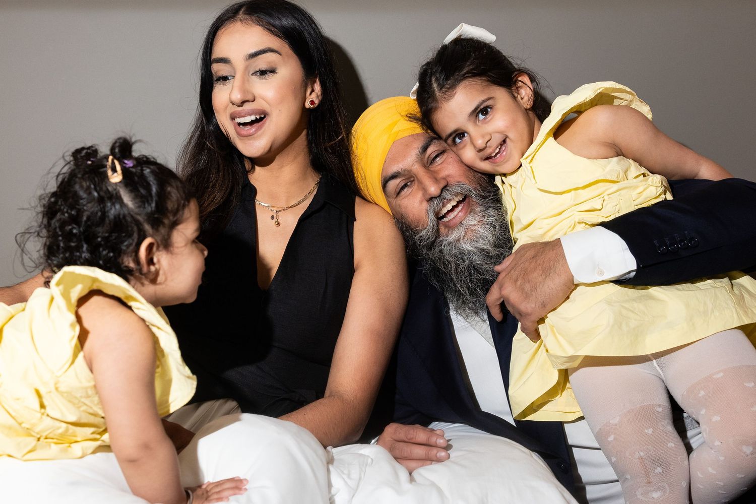 A young brown family with a mom, dad, and two daughters, laughing together. Bright hard flash.