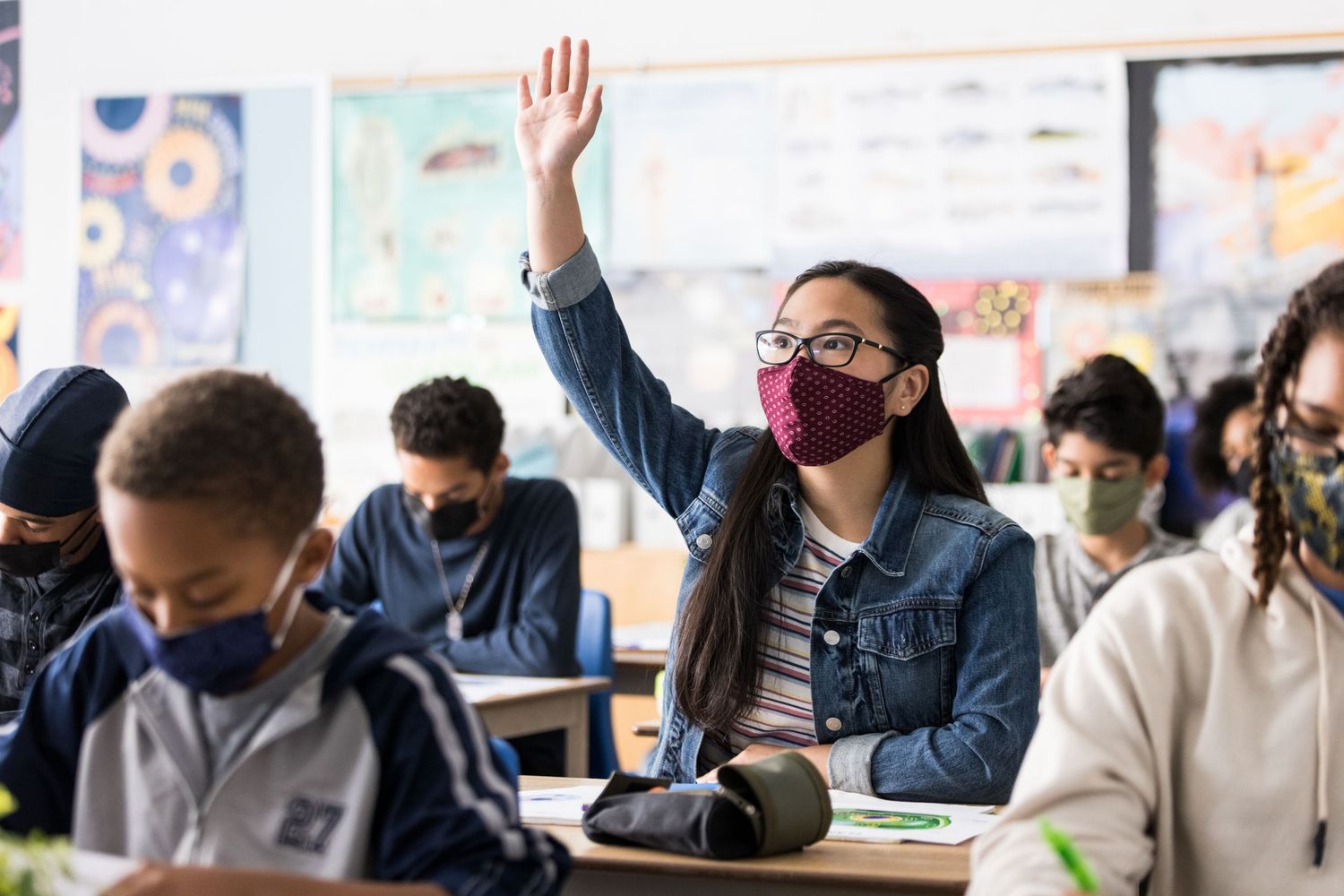 A young asian girl raises her hand in a busy classroom. Commercial lifestyle photography.