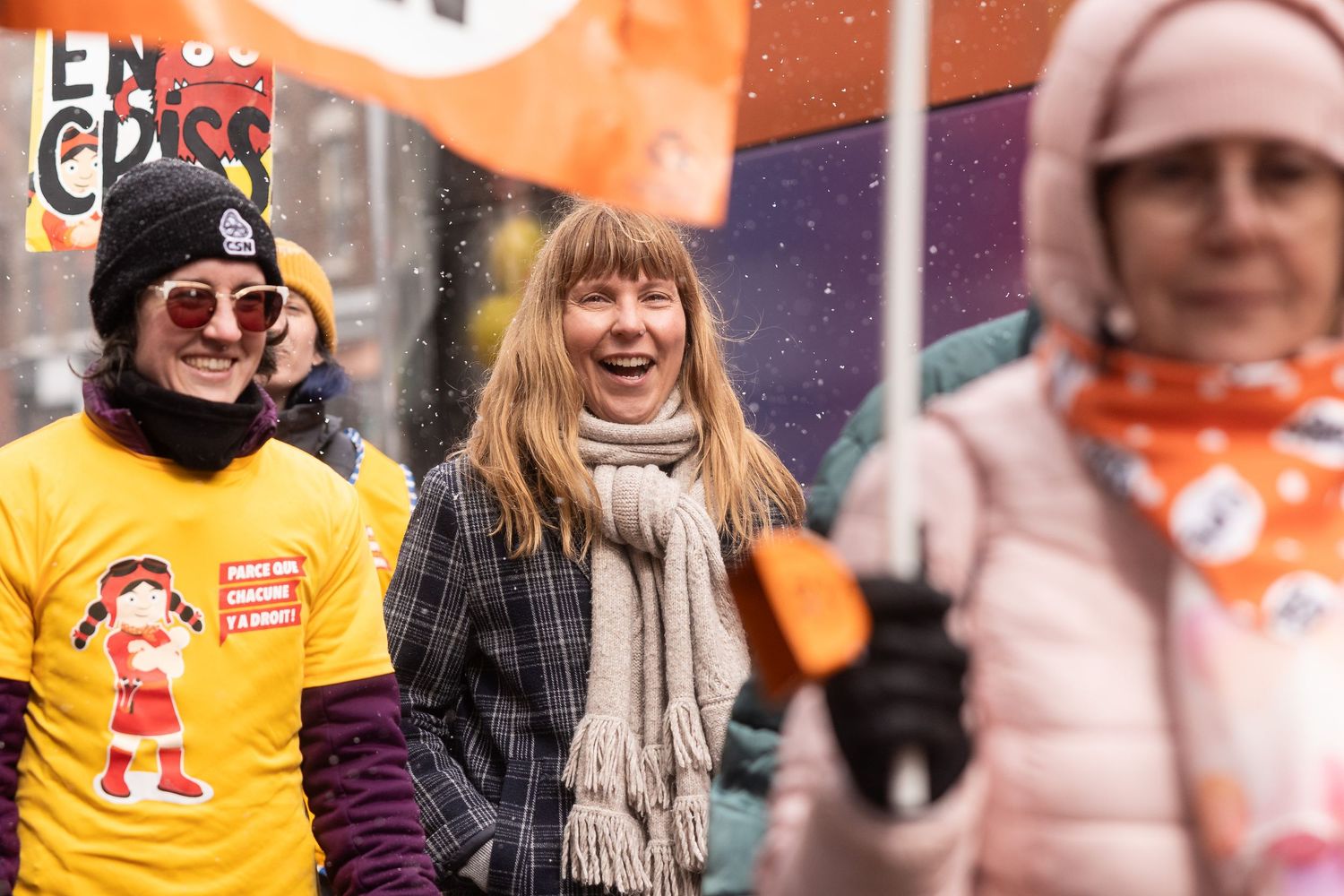 A group of union activists march outside smiling while on strike in the snow