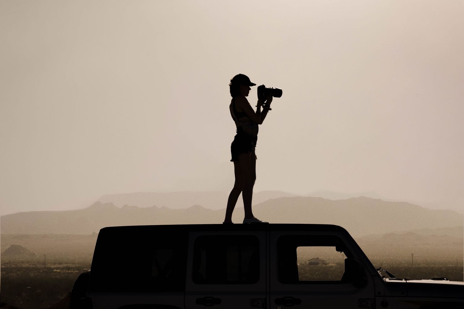 A person with a camera stands on top of a keep in the desert taking a photo. Adventure travel documentary photography