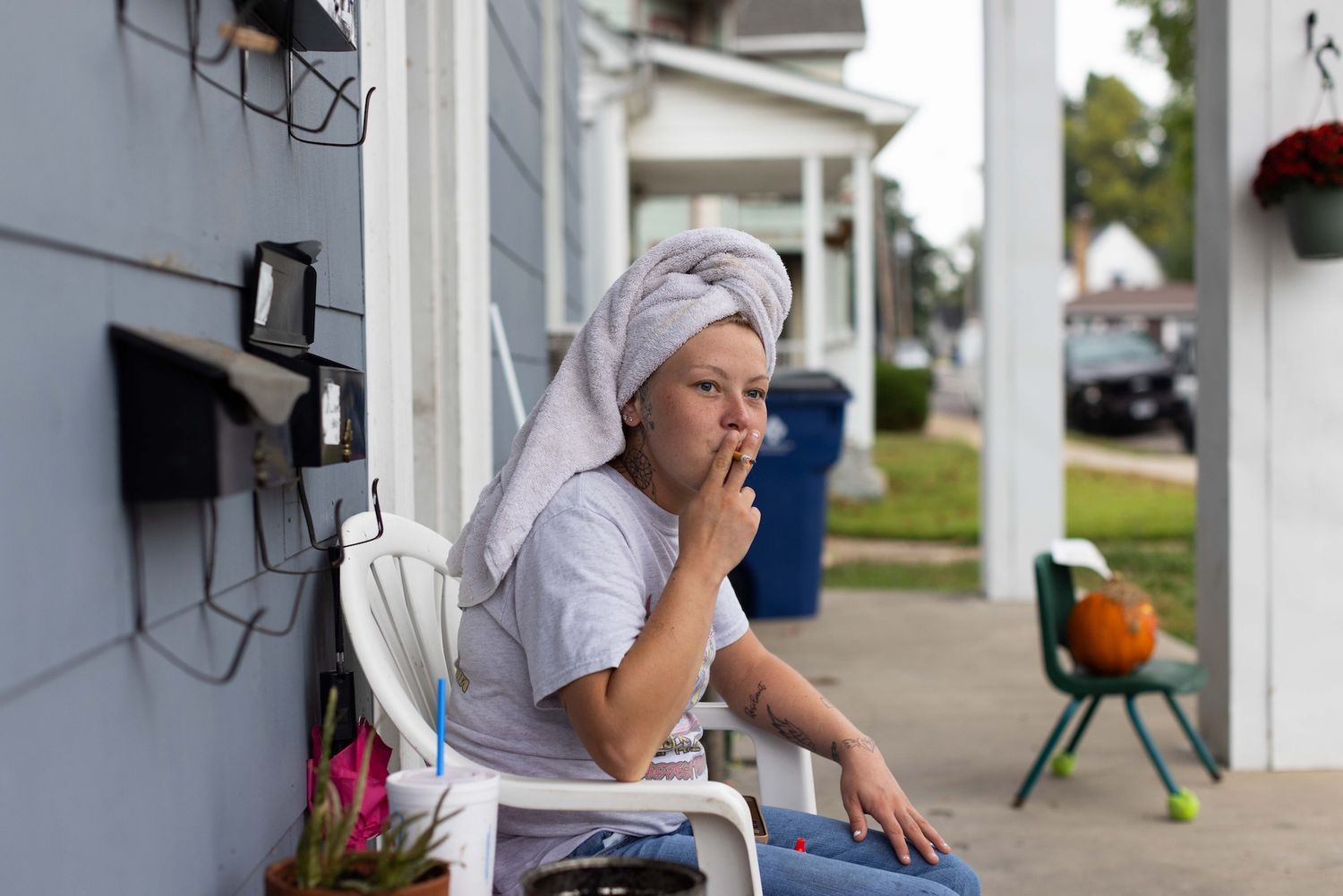 A young woman recovering from meth addiction sits outside having a cigarette with a towel on her head in the morning