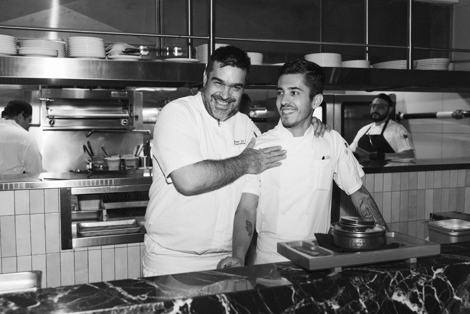 Two chefs laugh in the kitchen of their restaurant, black and white documentary photography