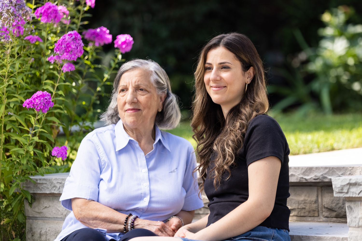 A grandmother and granddaughter sit on their front step at home. Commercial lifestyle photography for insurance, banking, families.