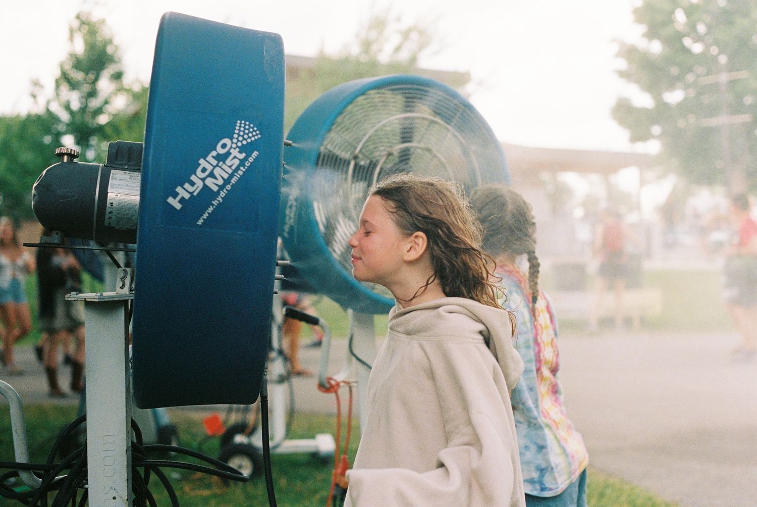 A young girl cools off in front of a cold water fan at a music festival