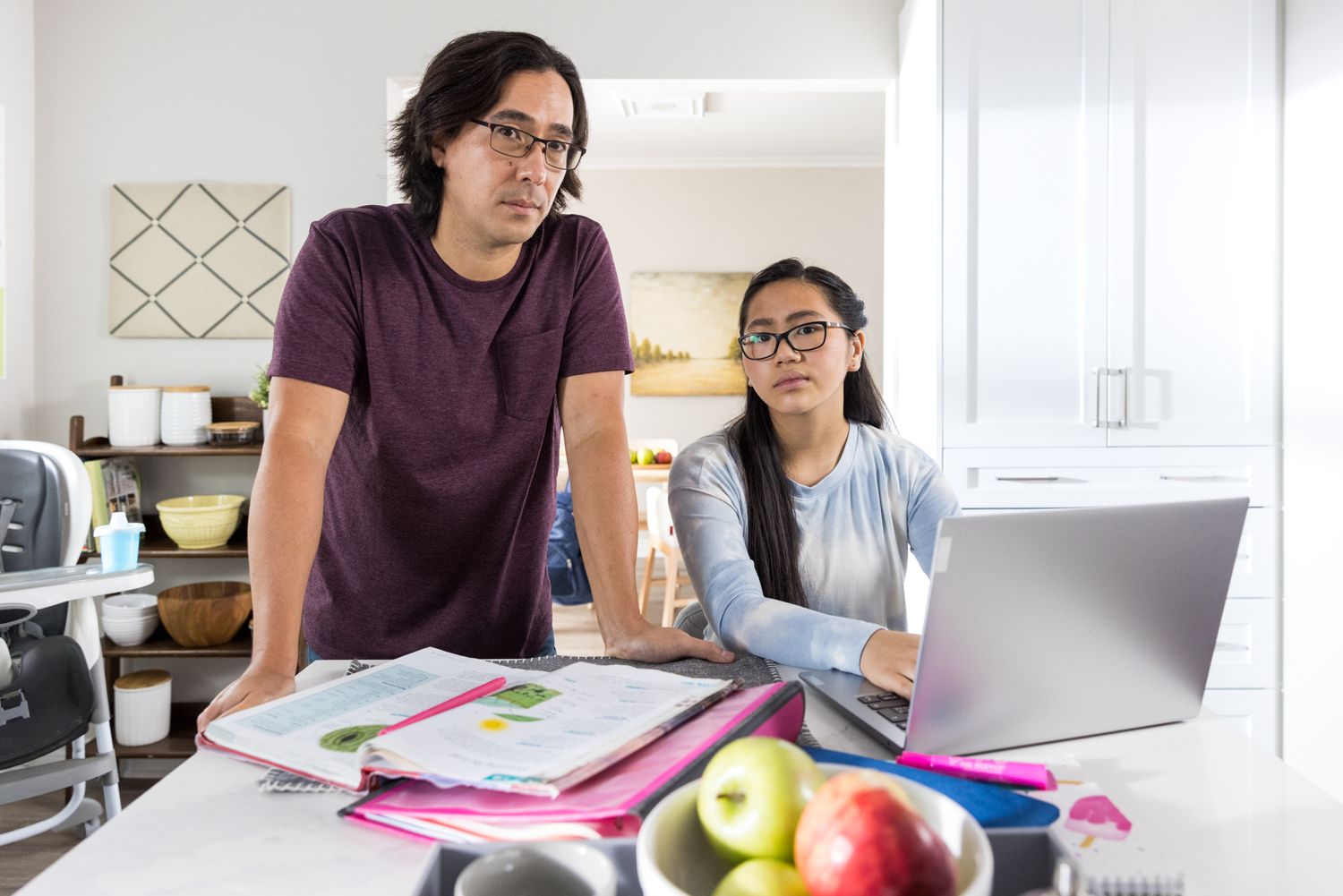 A father and daughter sit at the kitchen table confused, looking into camera. Commercial editorial photography for education and family