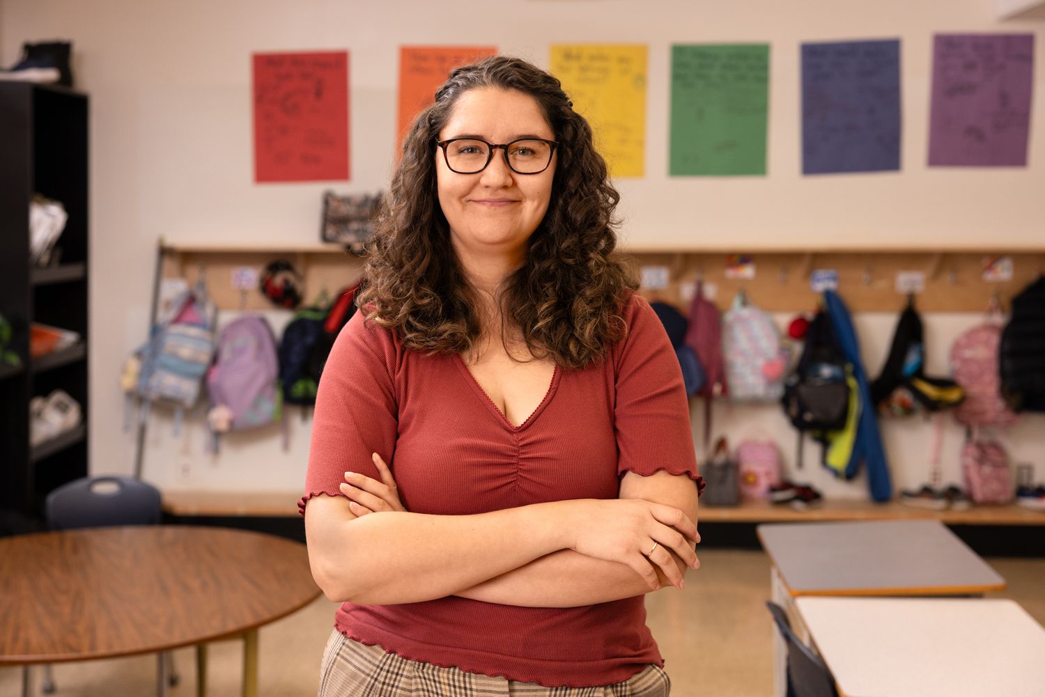 A young teacher smiles, arms, folded, in the classroom. Commercial lifestyle photography, back to school, teachers, families.