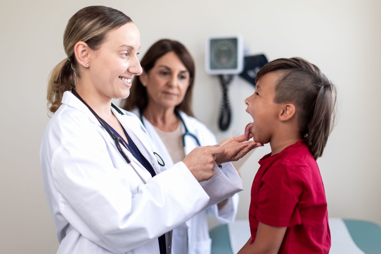 A female doctor examines a child while the mother watches smiling. Commercial lifestyle photography, medical, family, doctors