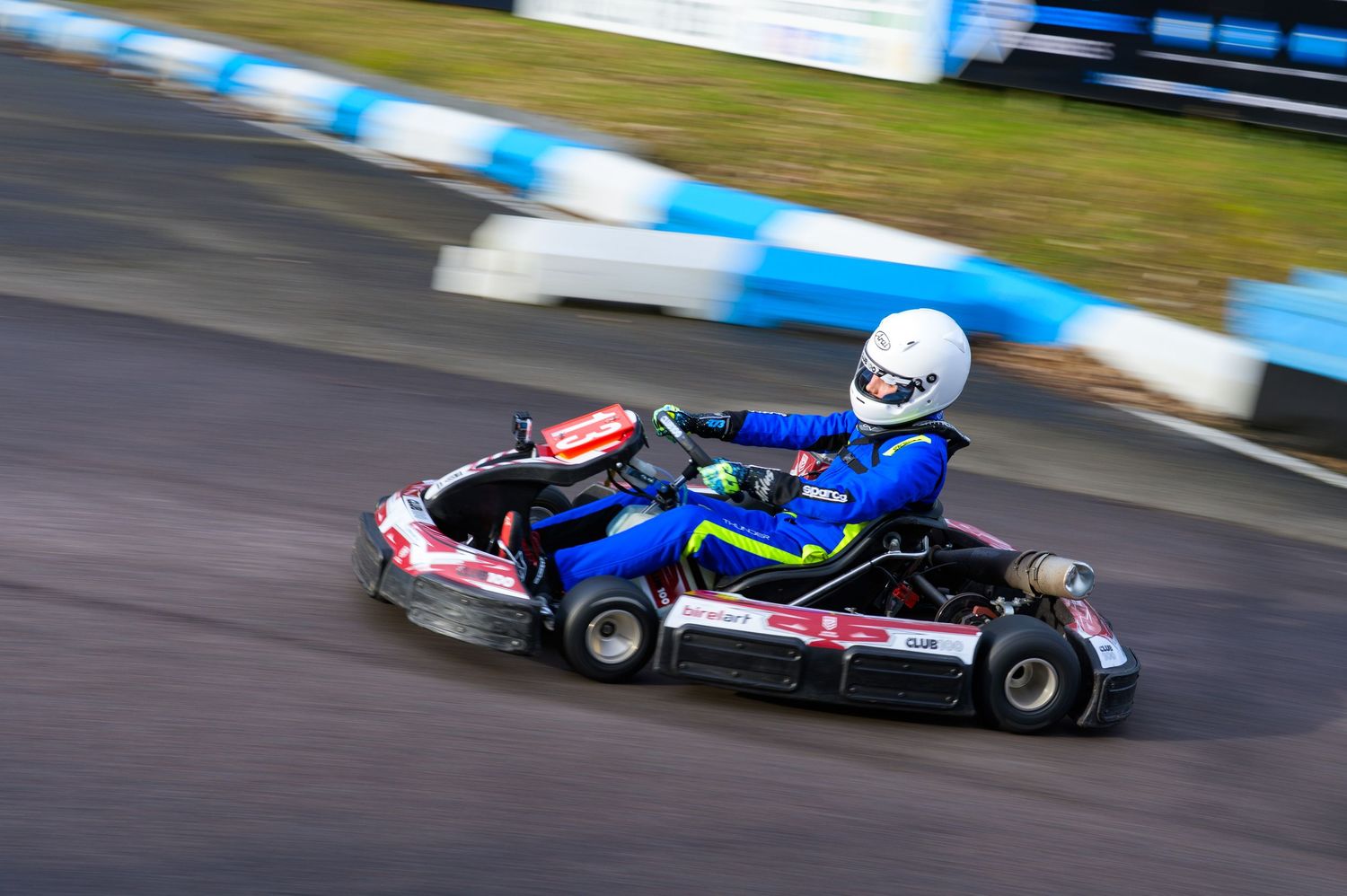 Multiple go karts navigate a curvy race track with red and blue barriers in daytime conditions.