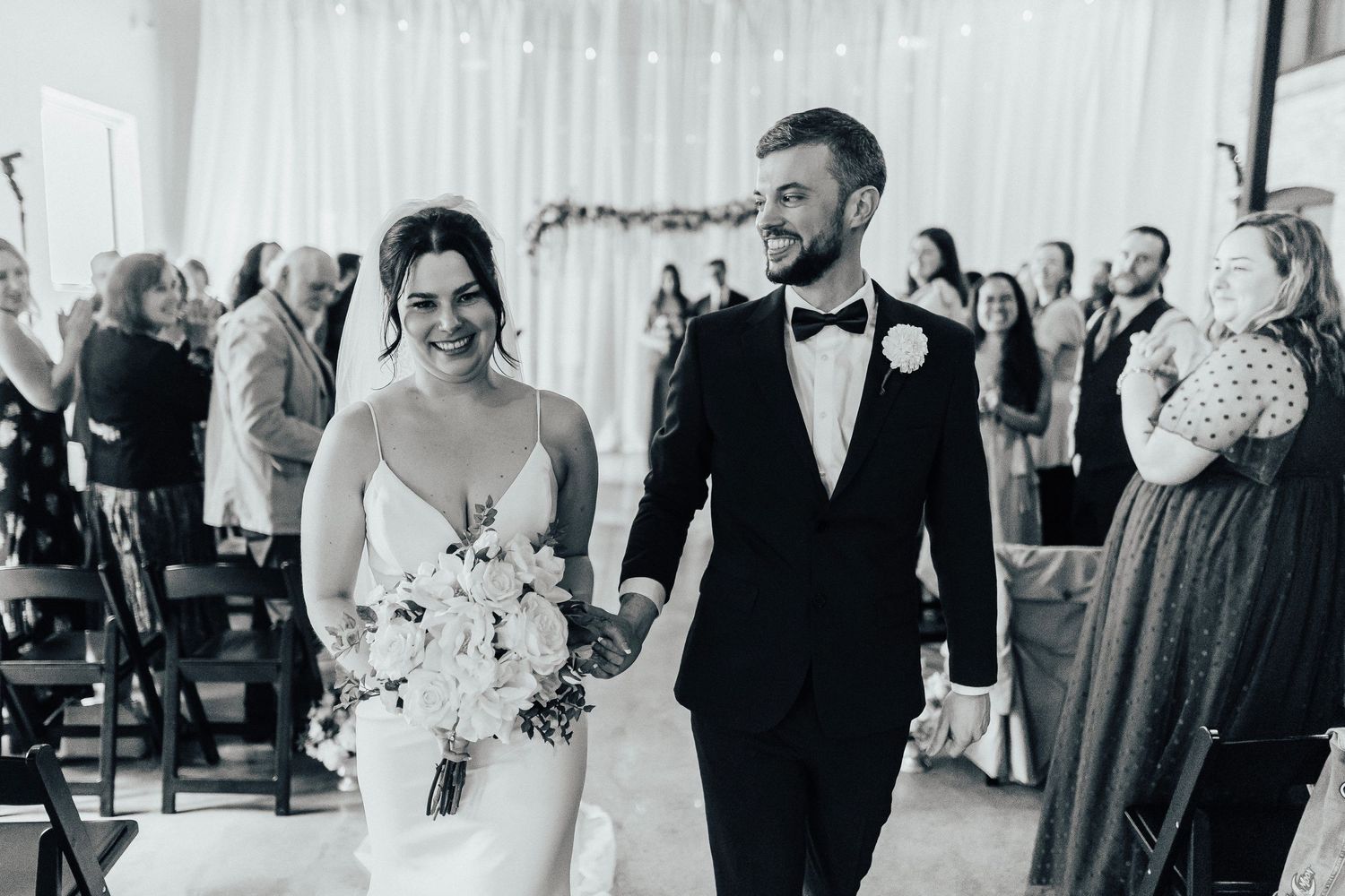 A newlywed couple walks down the aisle at their black and white themed wedding ceremony with guests in attendance.