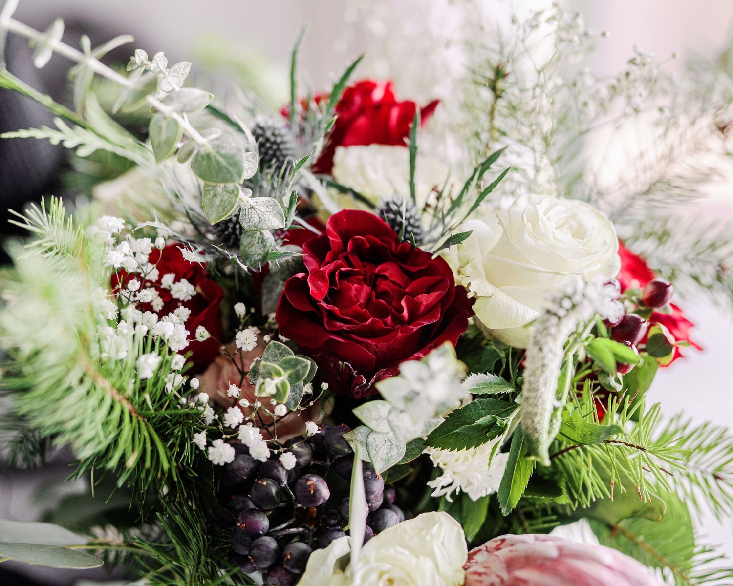 A winter wedding bouquet with deep red roses, white flowers, and evergreen pine branches with silver accents.