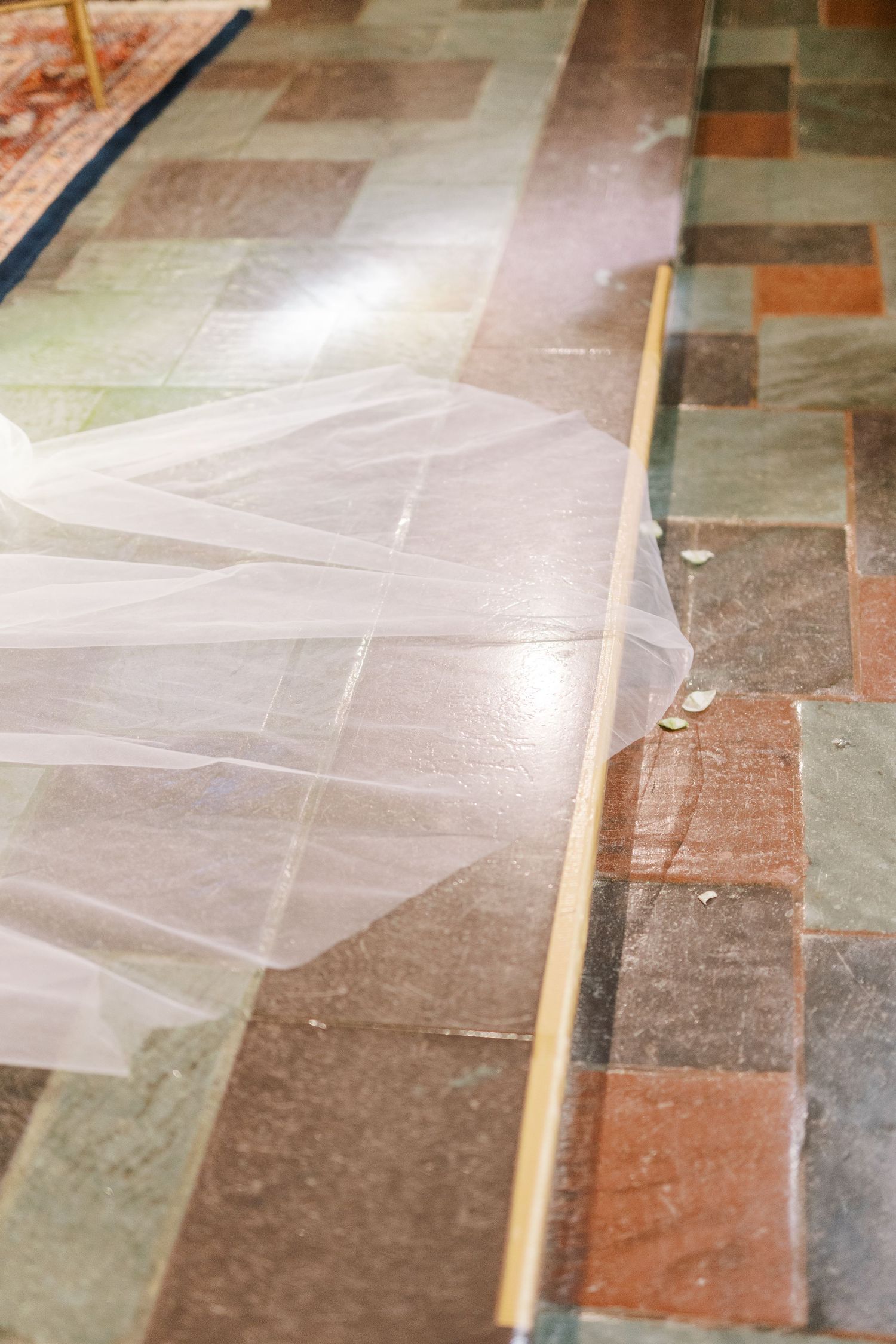Long flowing white wedding veil trailing across a multicolored stone church floor.