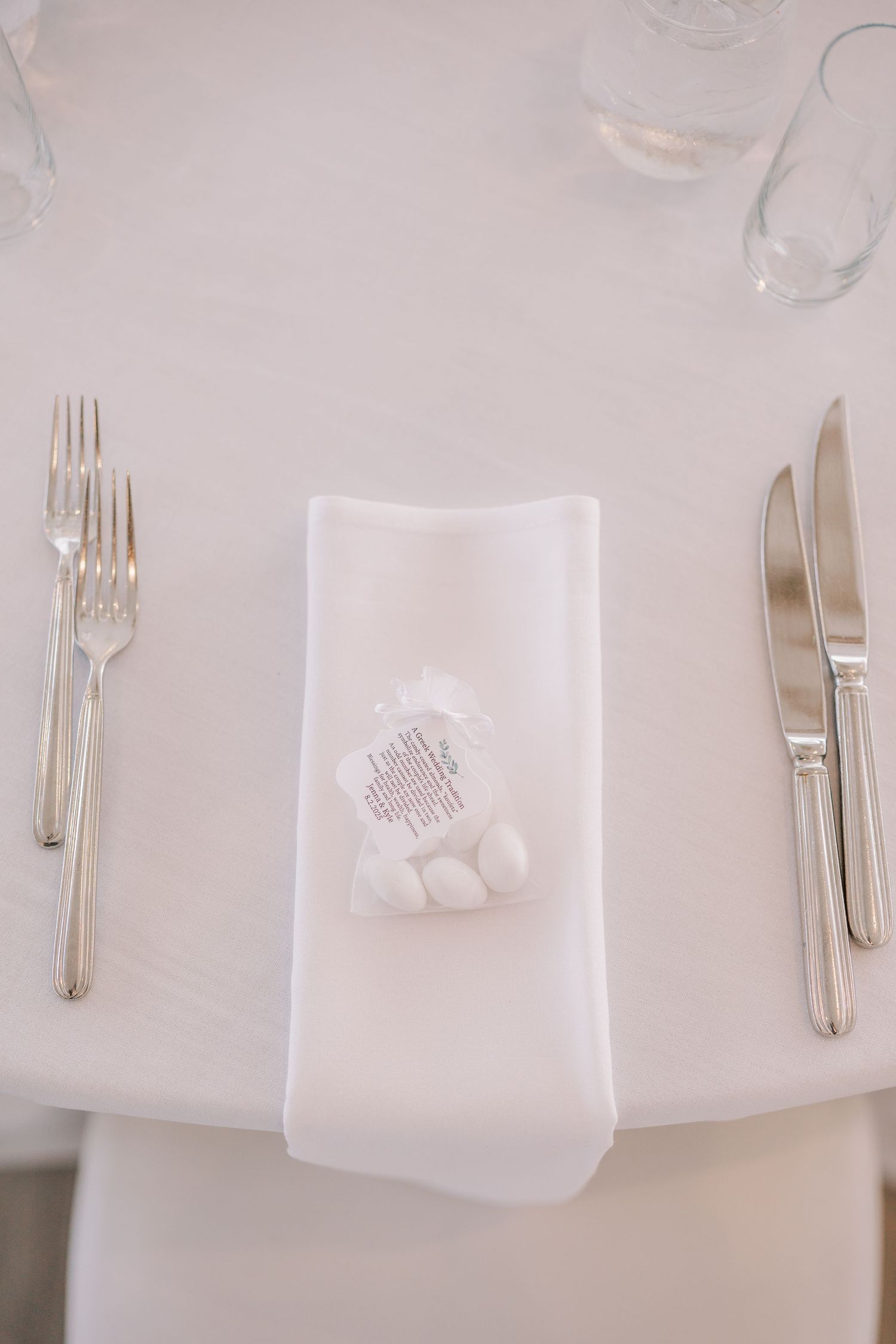 Elegant white table setting with folded napkin, silverware and small decorative favor at an upscale event.